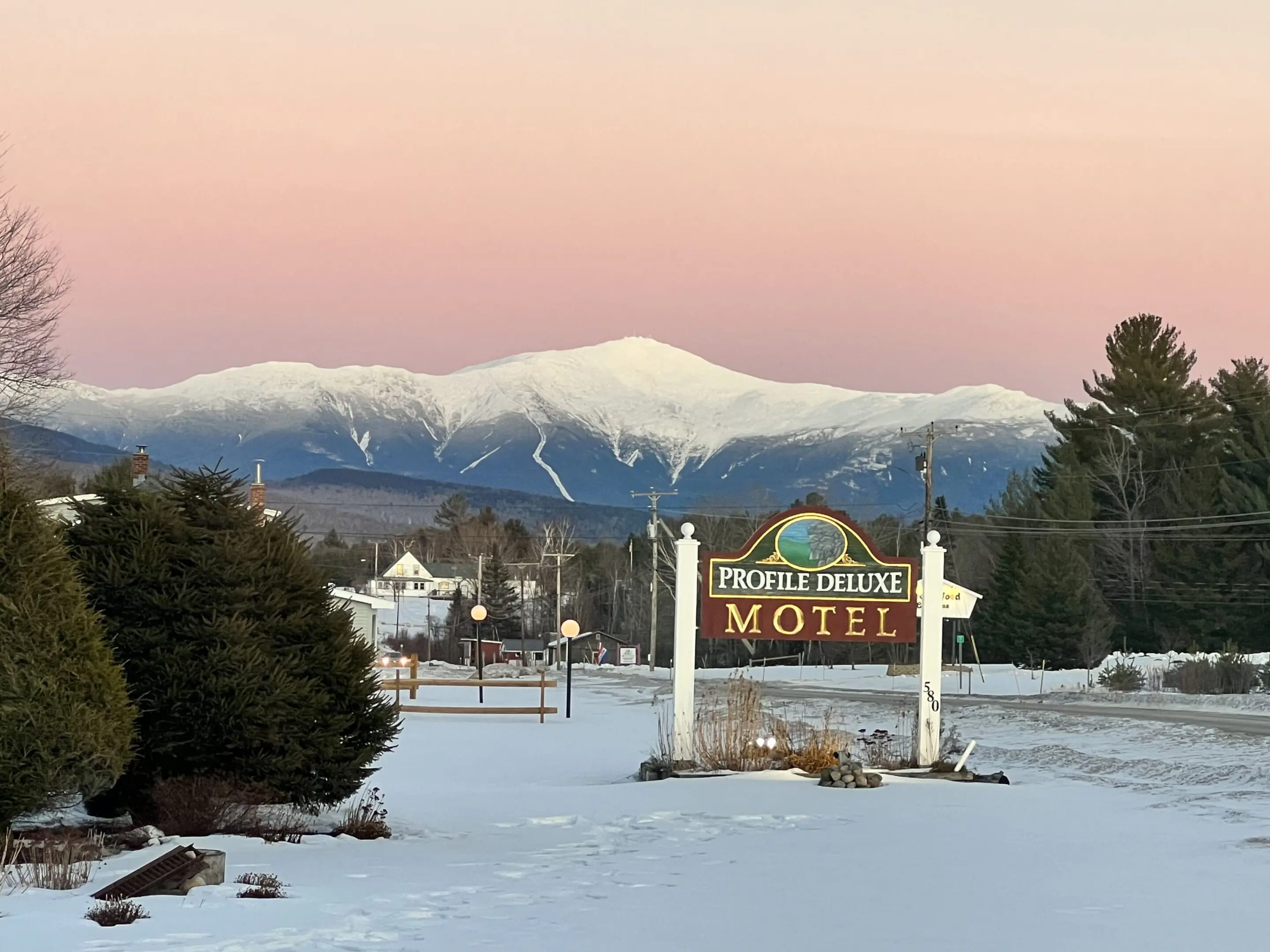 A motel sign in the snow with mountains behind it.