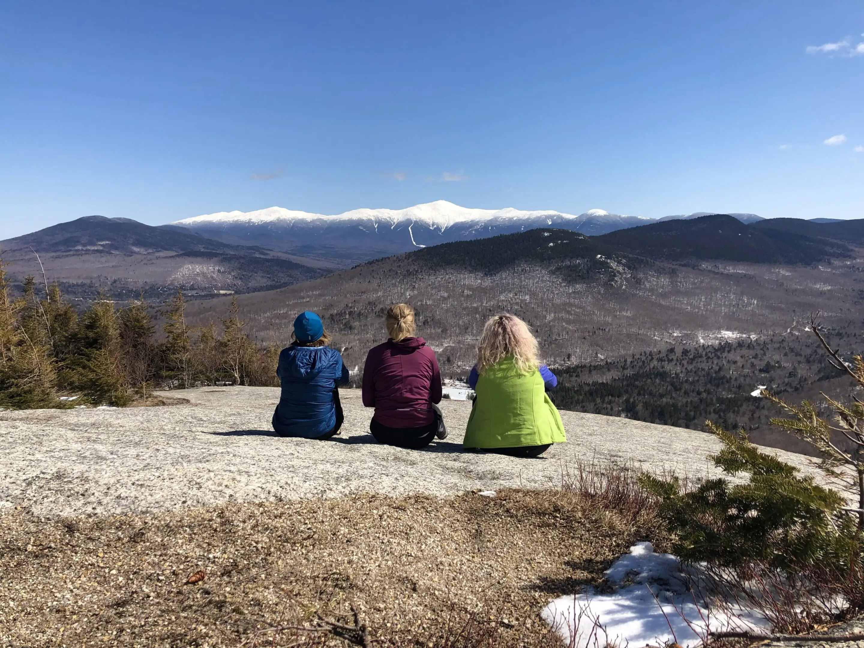 Three people sitting on a rock overlooking the mountains.