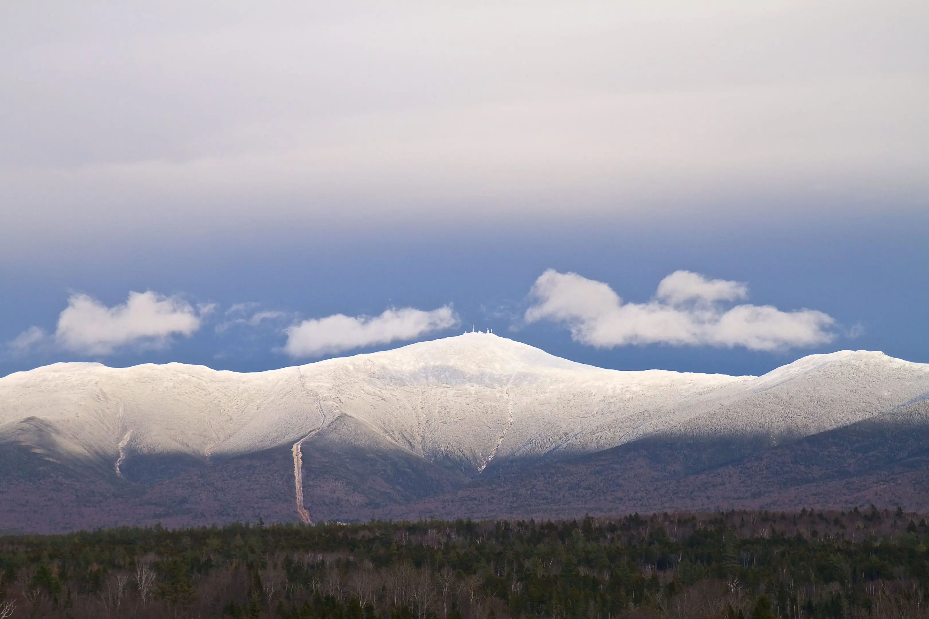 A cloud filled sky over the mountains with trees in the foreground.