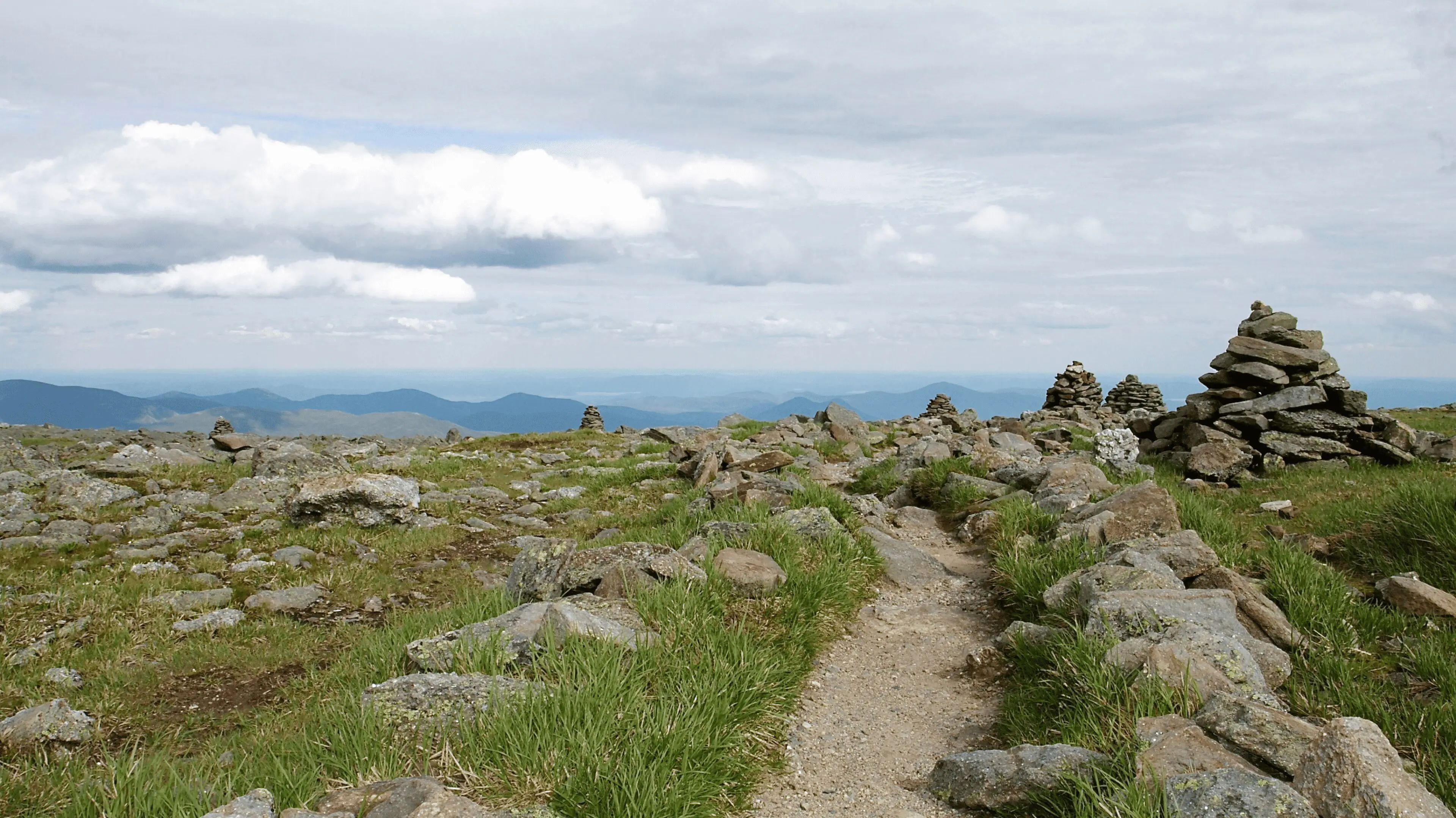 A trail on the side of a hill with grass and rocks.